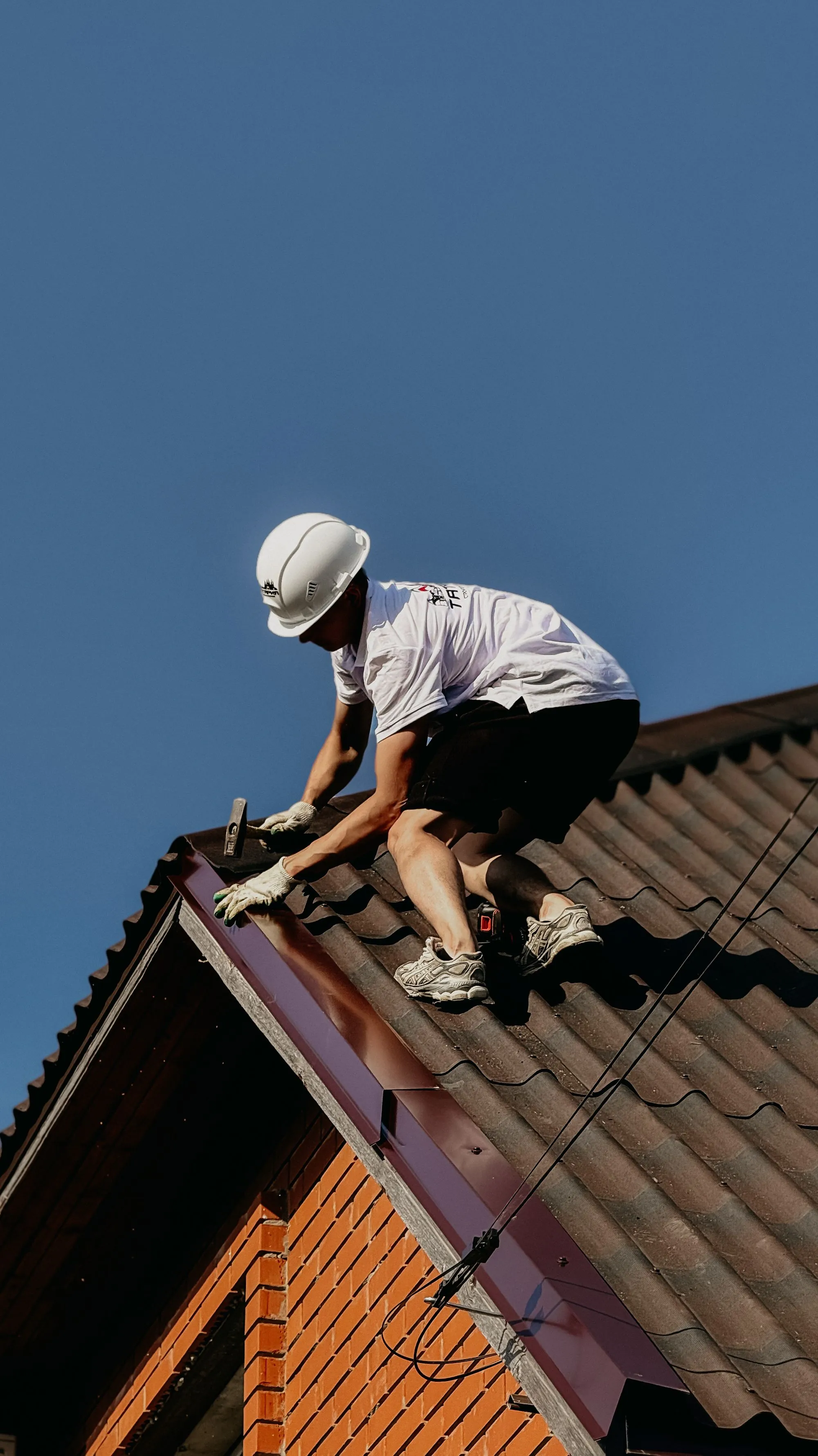 A roofer working along the edge of a roof against a clear blue sky