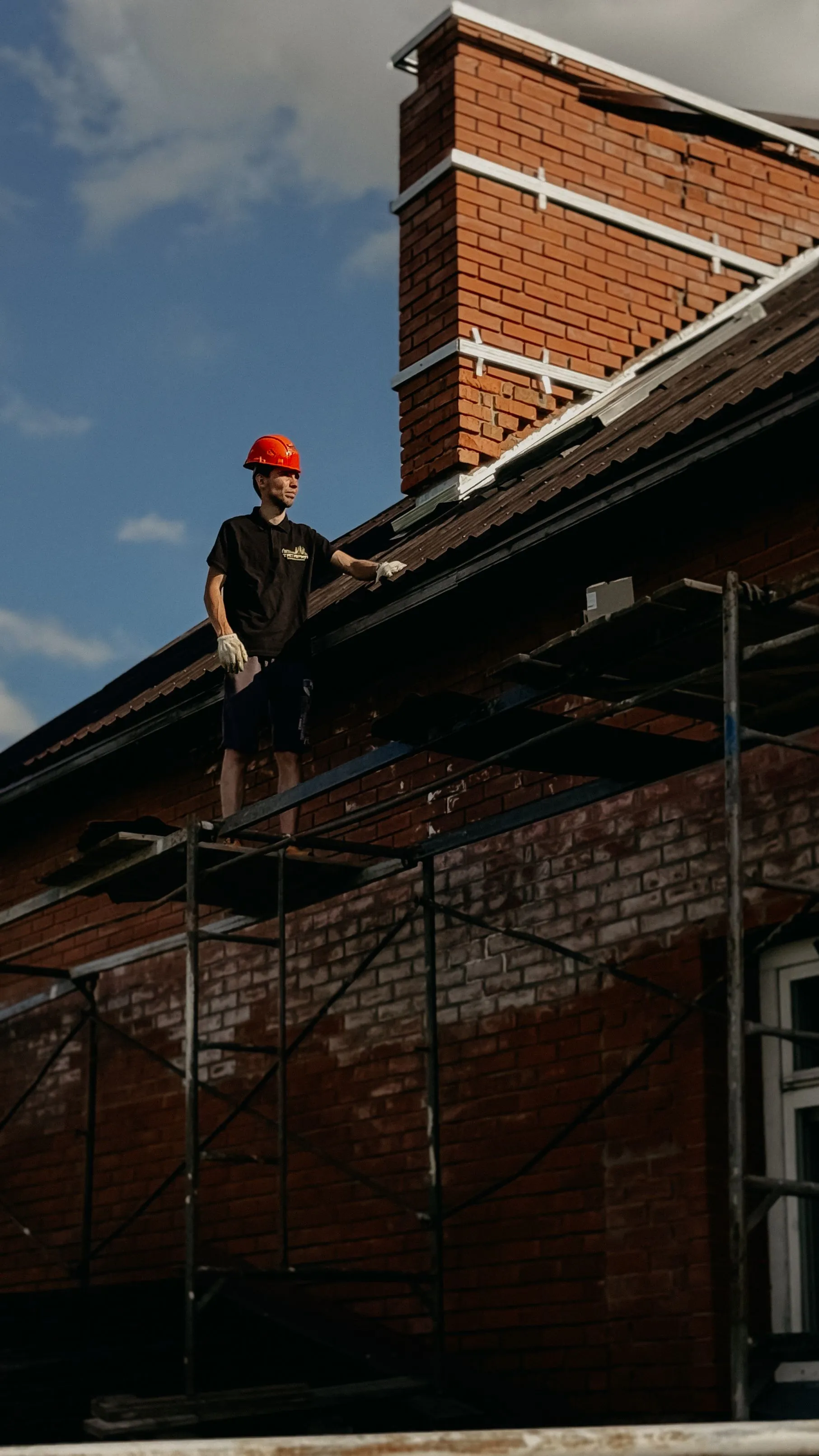 A roofer on scaffolding beside the brick gable of a house