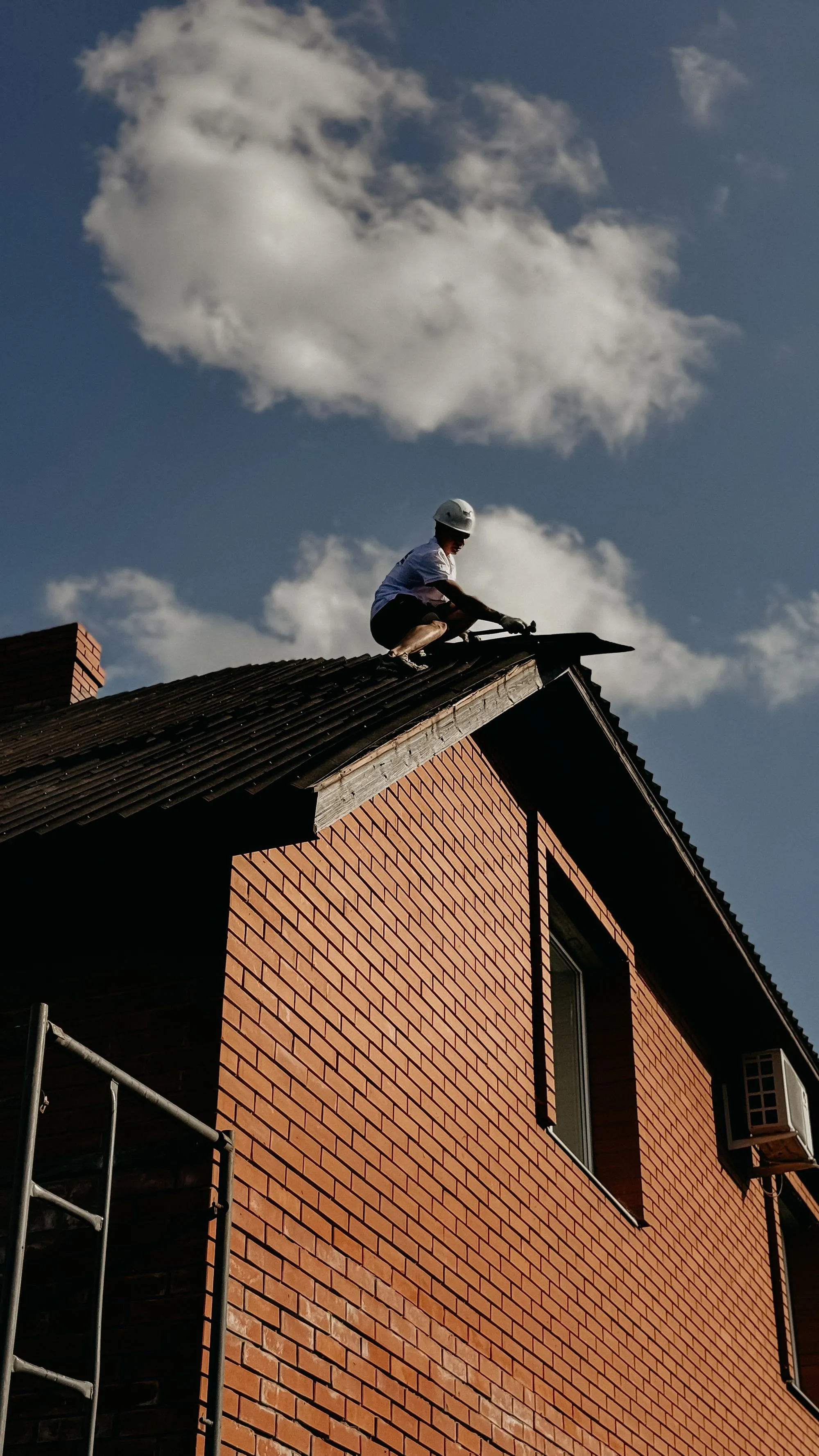A roofer standing on the ridge of a brick gable during a survey