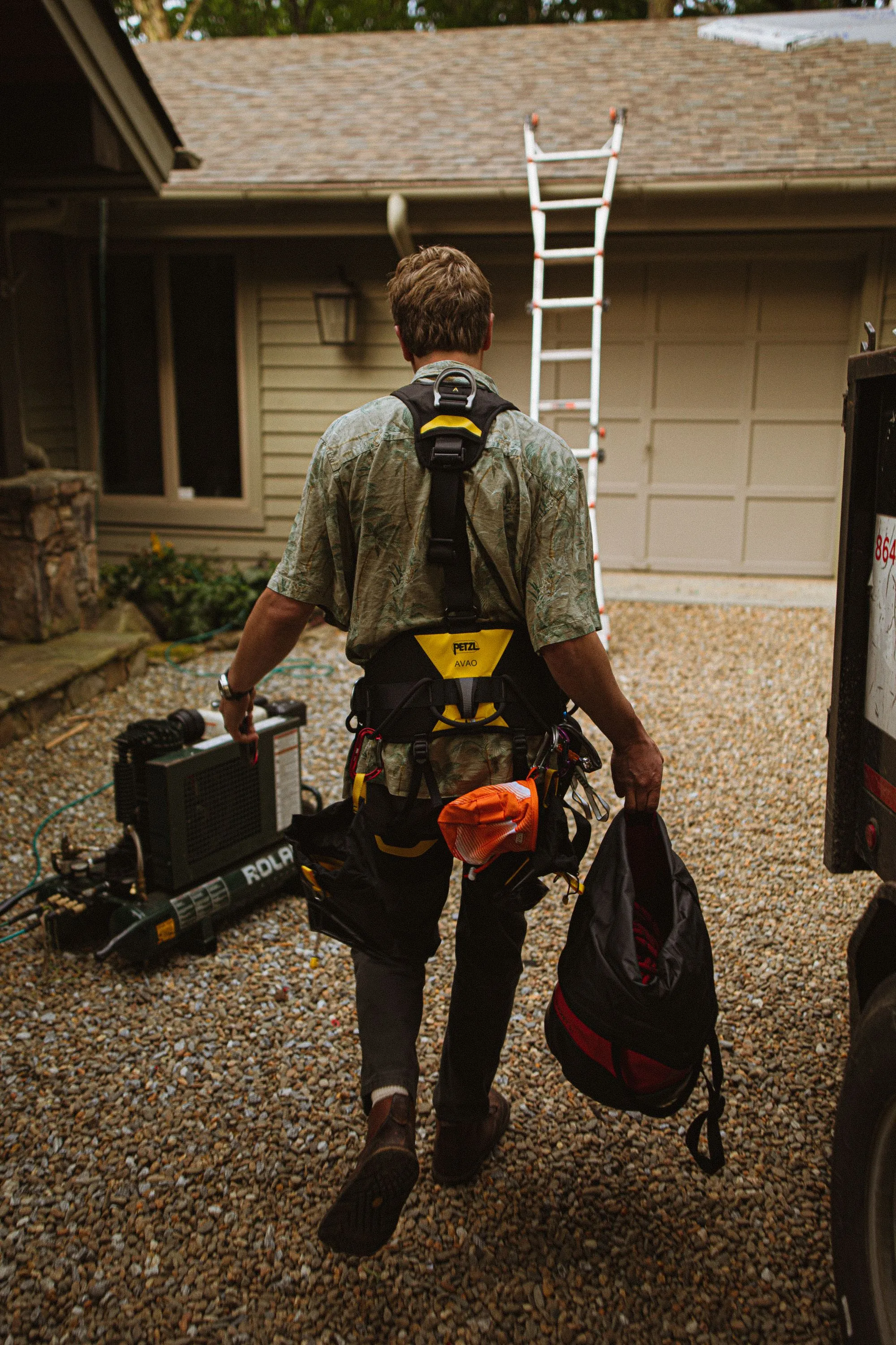A roofer carrying tools away from a house with a ladder still set against it