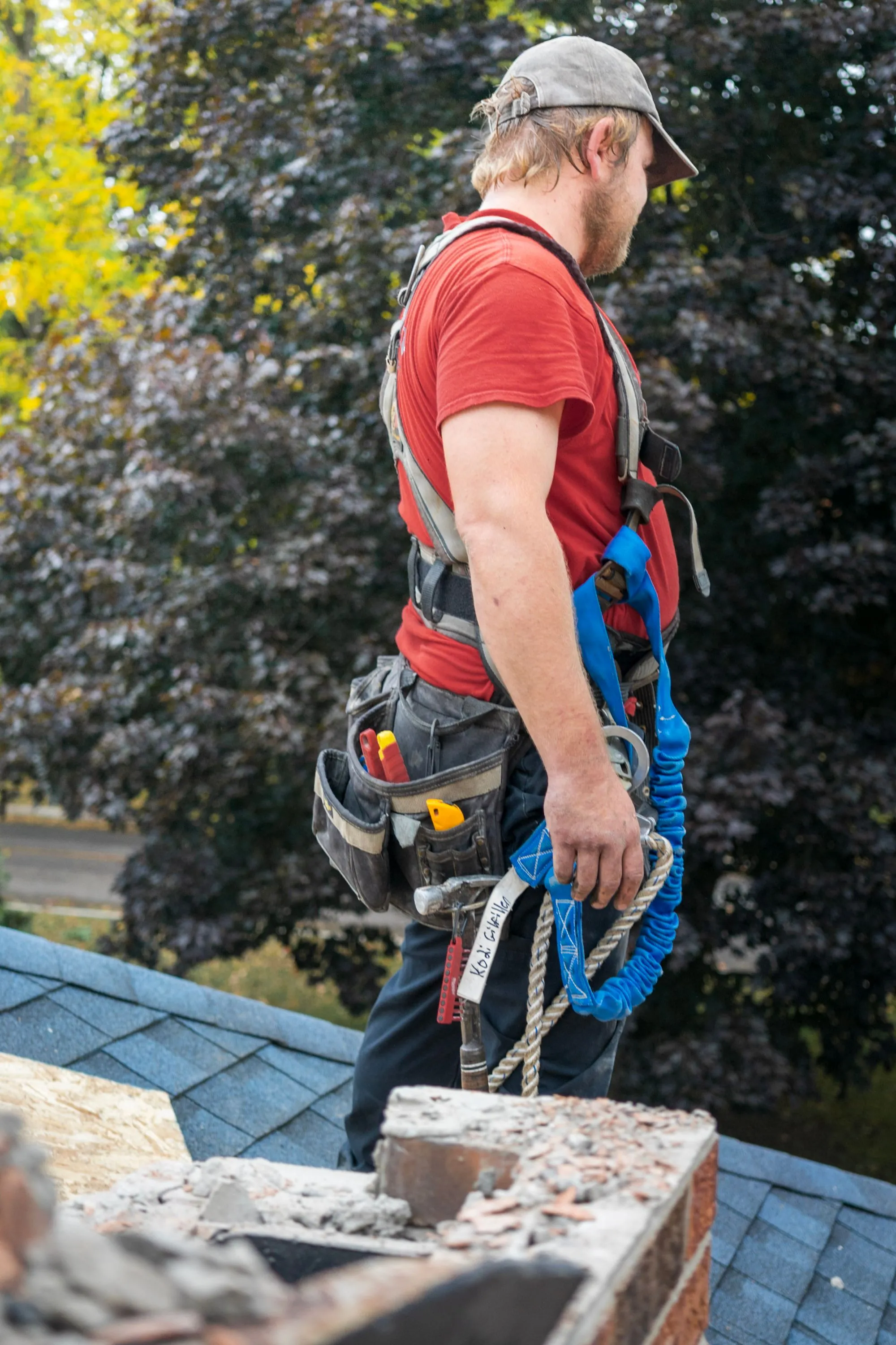 A roofer in safety gear working a rope line on a residential roof