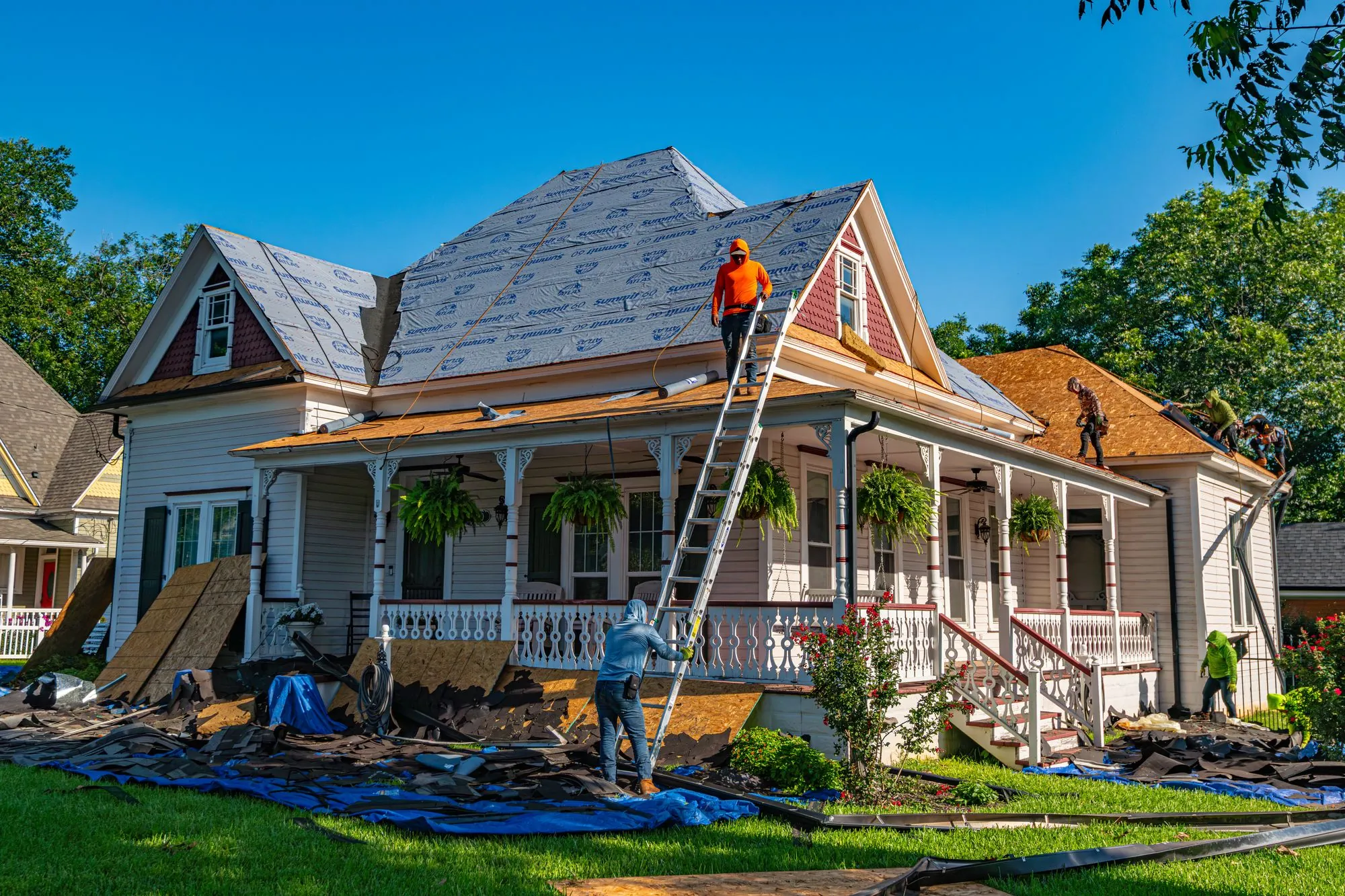 A ladder set against a porch roof as a crew re-covers a two-storey house