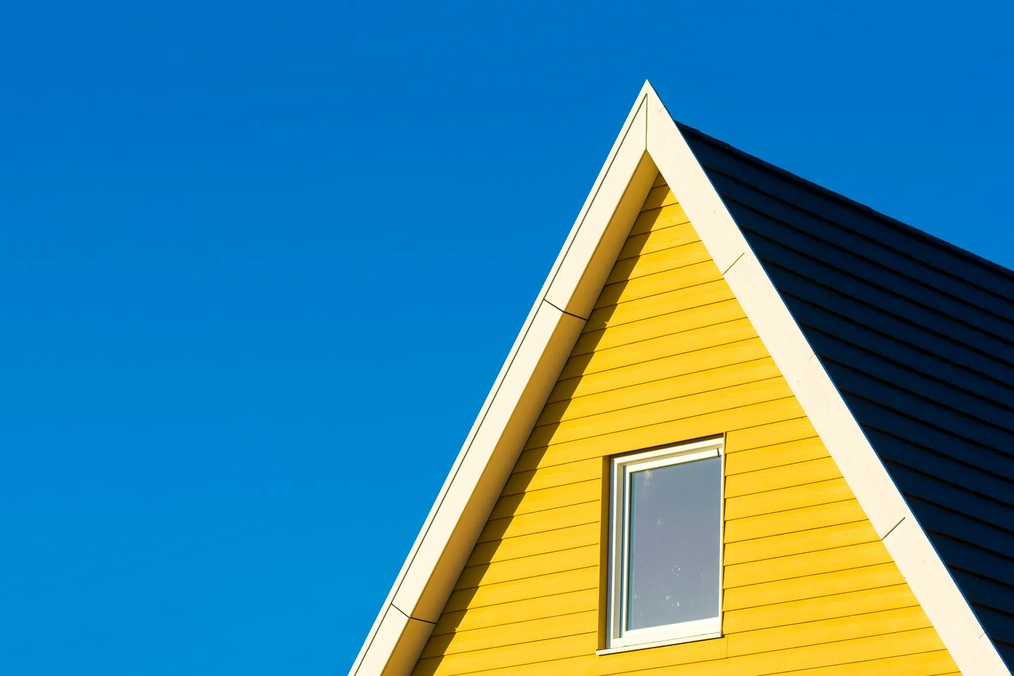 The lap-sided gable end of a house meeting a clear blue sky