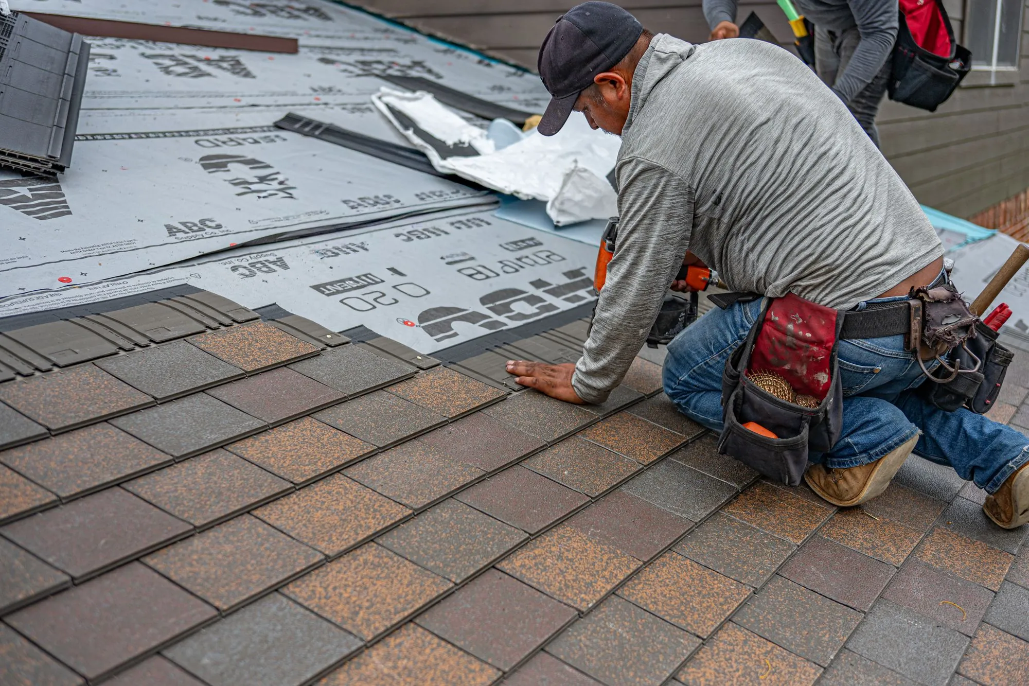 A roofer setting a course of asphalt shingles over fresh underlayment